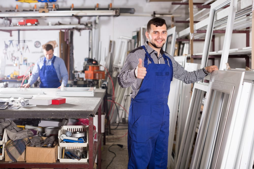 Worker inspecting aluminium doors and window frames in workshop. 