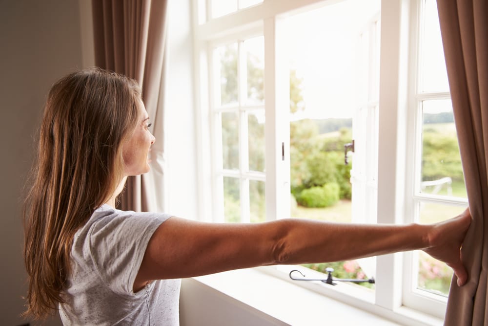 Woman Standing by Bedroom Window and Opening Curtains. 